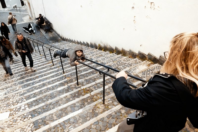 A child balances across a stair railing as pedestrians climb the stone steps.